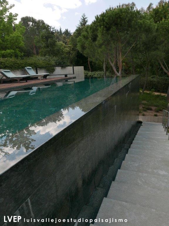 Piscina desbordante, vaso y muro desbordante, chapado en granito negro encina, jardín privado (Madrid)